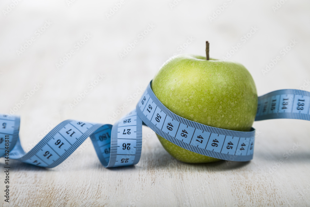 Green apple and measuring tape on a wooden table.