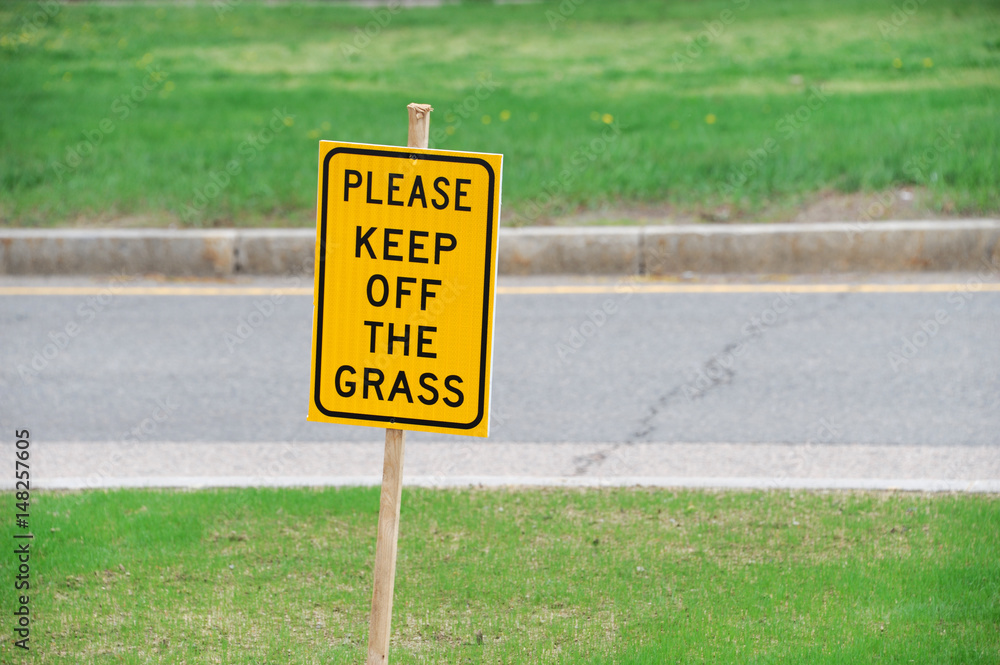 please keep off grass warning sign on the meadow along urban street