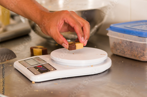 A man is using a food scale digital to weigh a cookie on metallic background