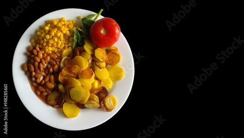 Fried potatoes, tomato, beans and corn on a white plate with uneven edges. Black background photo