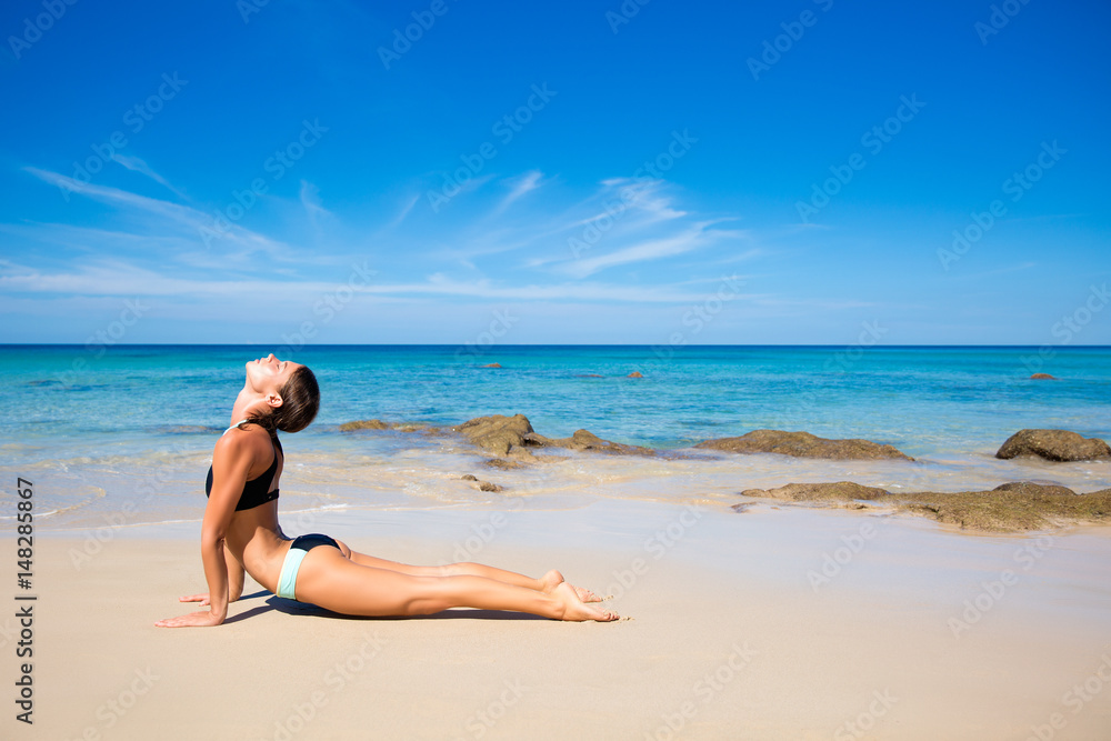 Healthy yoga exercise on the beach, slim sporty body training, leisure and meditation, vacation, sport, health care concept, over natural background blue sky and sea. Cobra pose