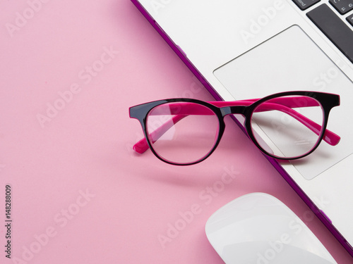 Flat lay, top view office table desk frame. feminine desk workspace with office accessories including laptop, pink glasses and mouse on pink background.