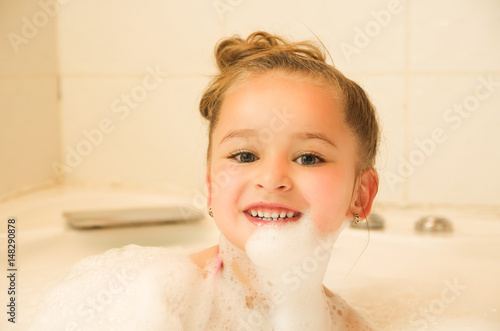 little beautiful girl posing inside of a bathtub with water and foam in bath