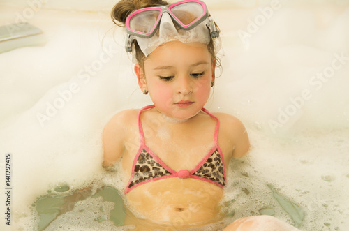 little beautiful girl playing with water and foam in bath using a swimsuit and beautiful dive sunglasses