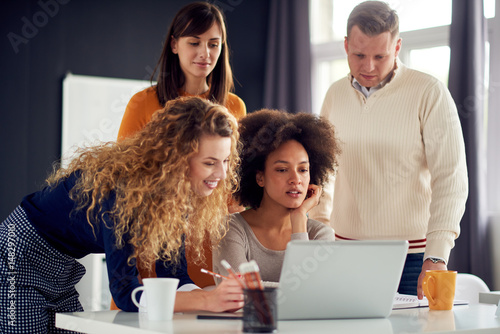 Young people working in modern office, discussing in front of laptop