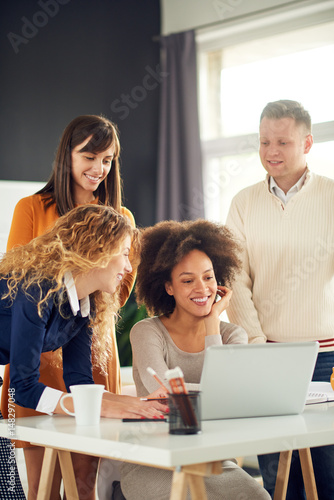 Young people working in modern office, discussing in front of laptop