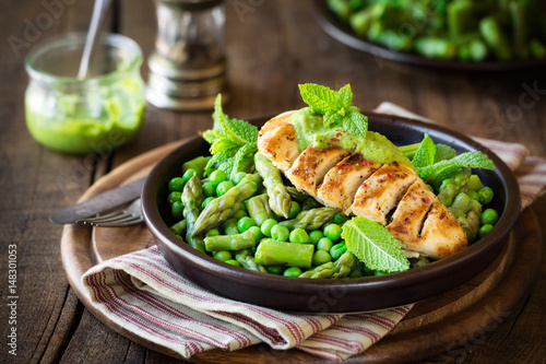 Delicious healthy homemade dinner with grilled chicken breast garnished with green peas, asparagus stalks and mint sauce against dark rustic background