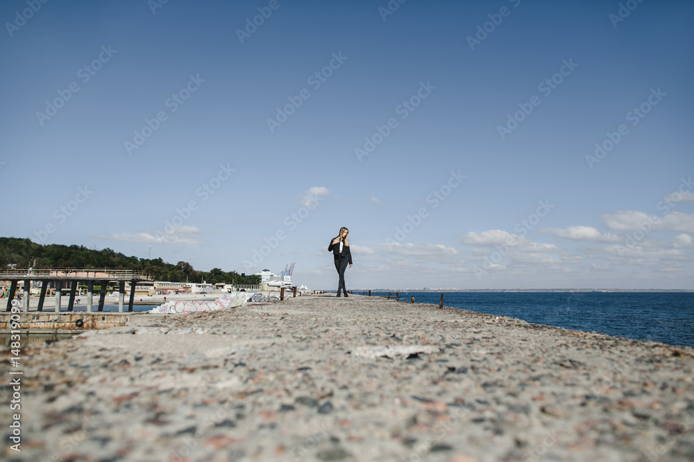 The stylish girl stands on the pier near sea