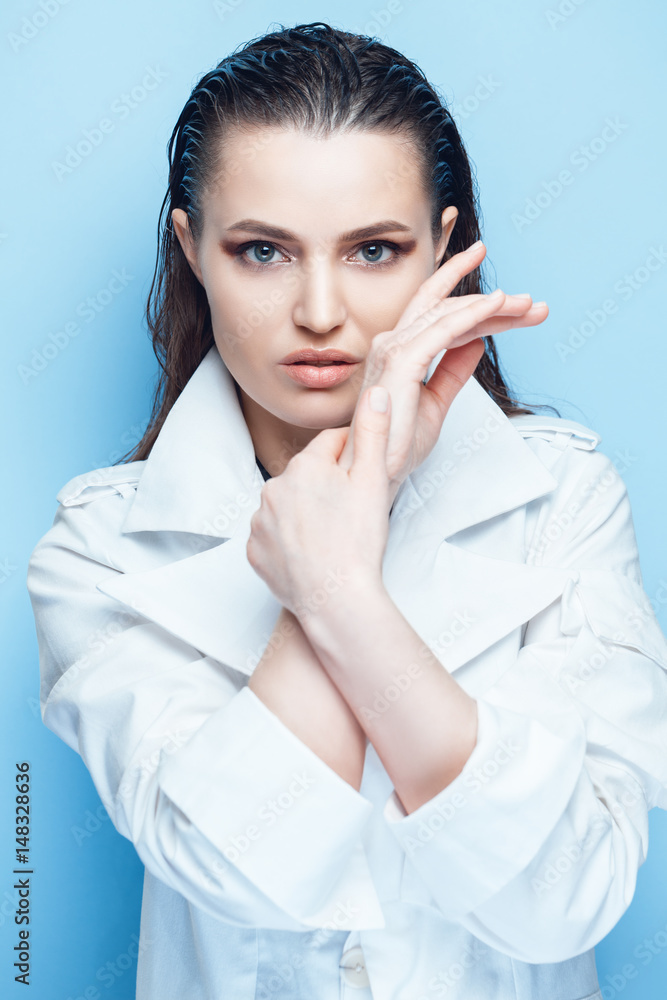 Portrait of a beautiful brunette woman with long hair posing on blue background in white coat Portrait of a beautiful brunette woman with long hair posing on blue background in white coat