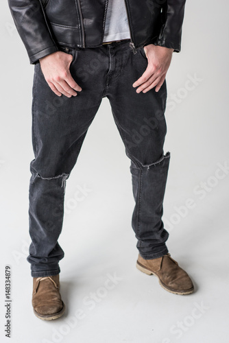 low section of young man posing in ripped jeans isolated on grey