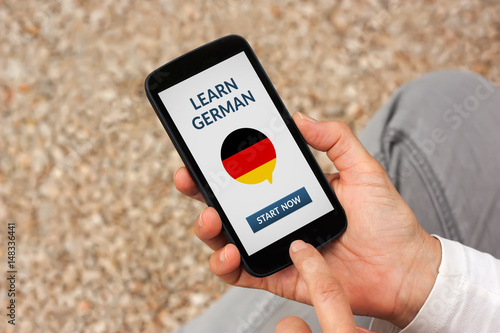 Hands holding smart phone with learn german concept on screen. All screen content is designed by me