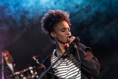 Female singer with microphone and rock and roll band performing hard rock music on stage photo