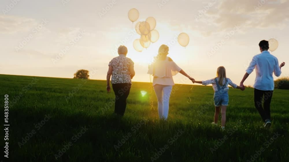 For several generations the family walks along the green meadow towards the sunset. Concept - family values, communication, happy childhood. Back view For several generations the family walks along the green meadow towards the sunset. Concept - family values, communication, happy childhood. Back view