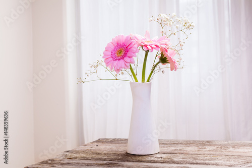 vacker bukett med rosa gerbera i vit vas på trä bord och vit gardin i bakgrunden photo