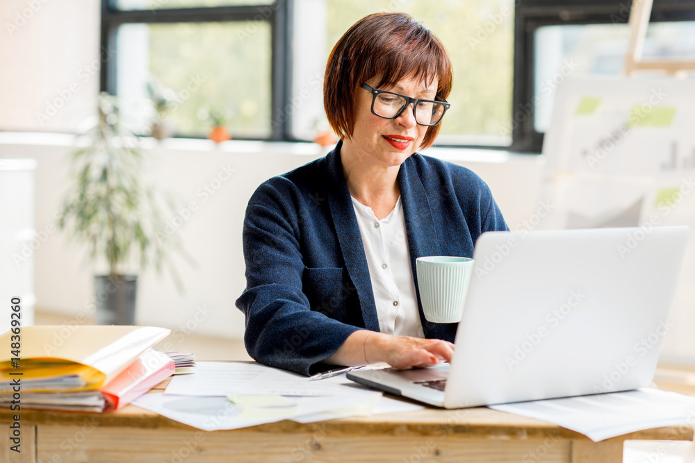 Portrait of a senior businesswoman working with documents and laptop at the bright modern office interior Portrait of a senior businesswoman working with documents and laptop at the bright modern office interior