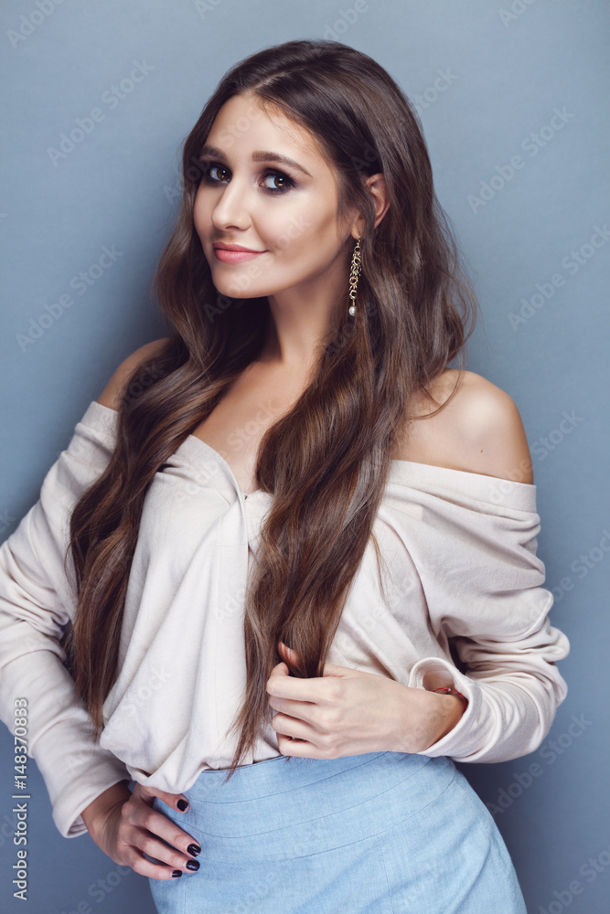 Portrait of a beautiful brunette girl with long wavy hair posing on pastel blue background Portrait of a beautiful brunette girl with long wavy hair posing on pastel blue background