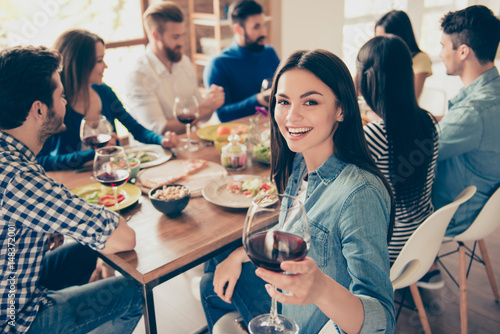 Close up of a girl looking at the camera holding glass of red wine and smiling. She is posing to photographer to memorise a moment of party