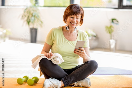 Konstfotografi Older woman using smartphone after sports training sitting indoors at home or gy