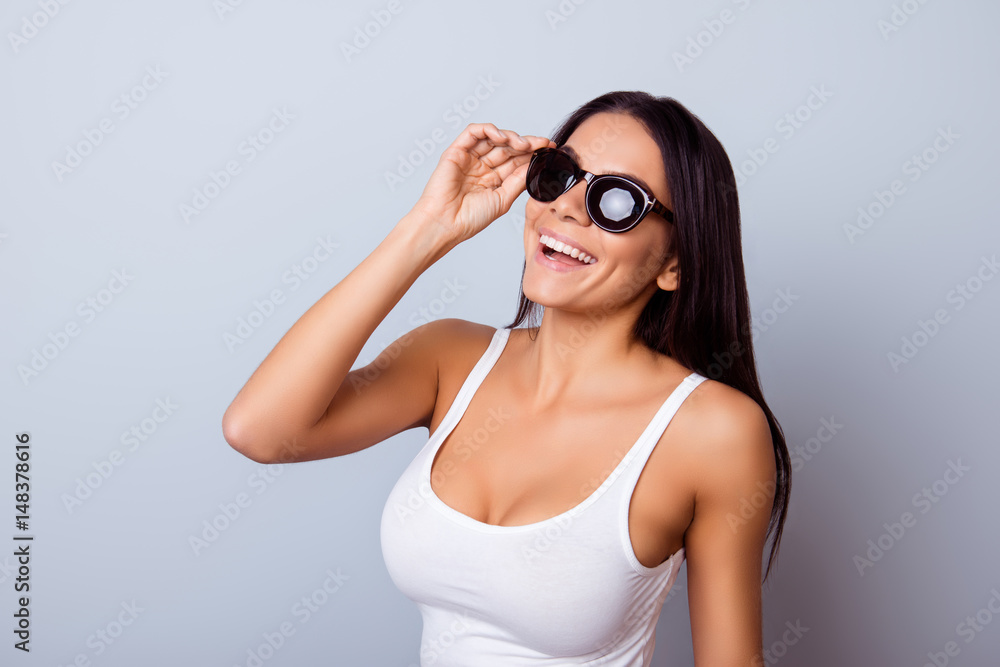 Young cute latin american lady with beaming smile in stylish spectacles is standing on the light blue background. She is full of dreams and fantasies