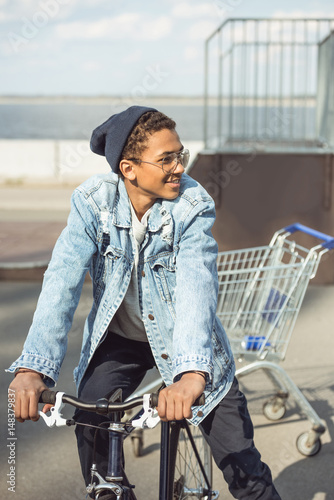 smiling hipster teenage boy riding bicycle at skateboard park