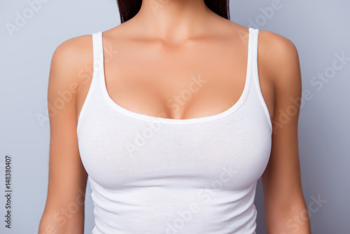 Close up of perfect lady`s chest with bronze skin in white singlet on light blue background