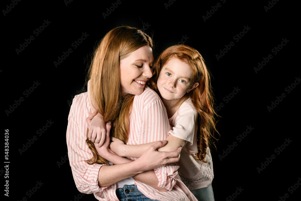 Beautiful happy redhead mother and daughter embracing isolated on black