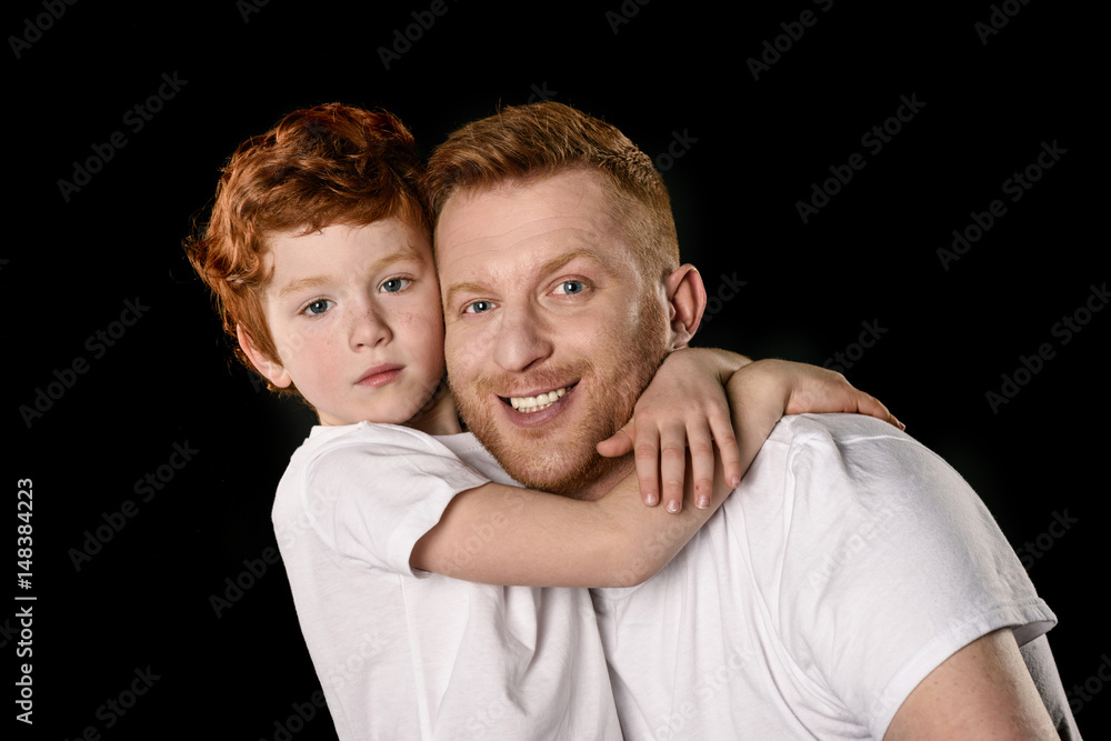 Happy father with son hugging and smiling at camera isolated on black Happy father with son hugging and smiling at camera isolated on black