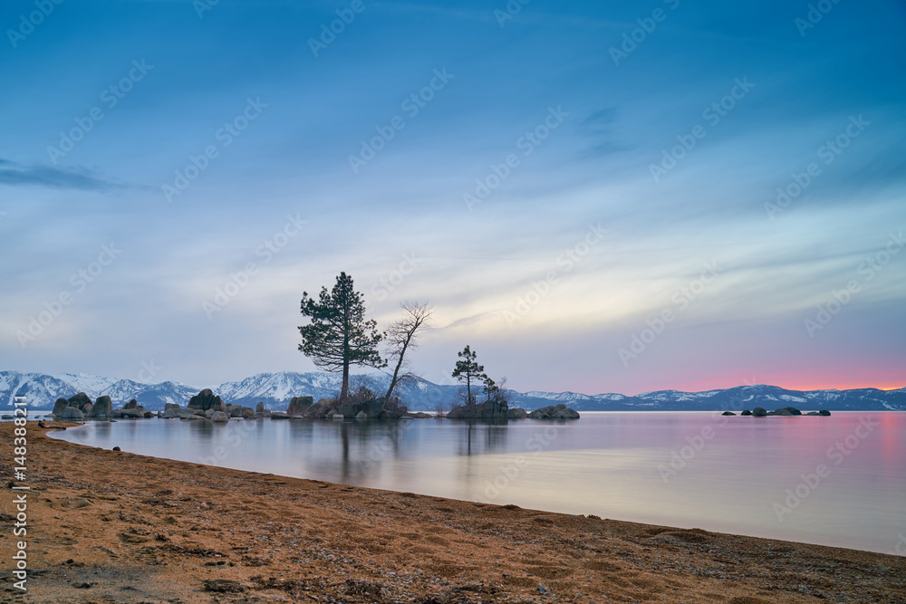 Sunset at Lake Tahoe with sand beach, mountains covered by snow at background