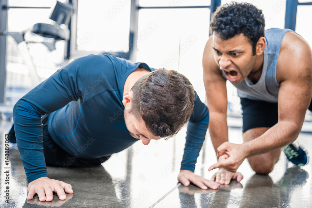 young man doing push-up and trainer yelling on him at sports center young man doing push-up and trainer yelling on him at sports center