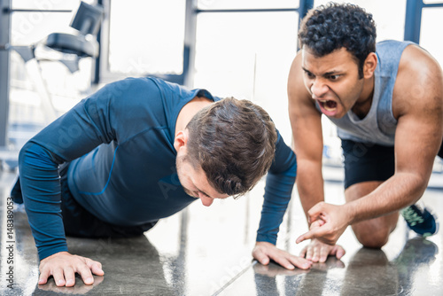 young man doing push-up and trainer yelling on him at sports center