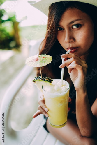 Young beautiful woman drinking cocktail with pineapple in beach bar