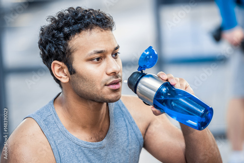 Handsome young man with bottle of water resting at gym