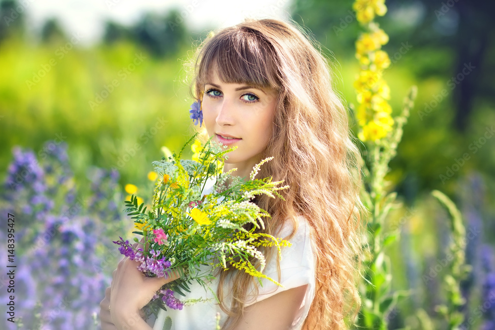 Portrait beautiful young the woman with a long fair hair who holds a bouquet of wild flowers Portrait beautiful young the woman with a long fair hair who holds a bouquet of wild flowers