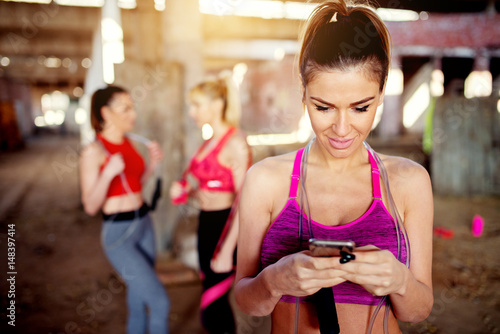 Beautiful young woman listening music fitness training workout. Group of fitness people behind preparing for training.