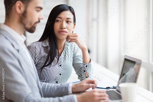 Portrait of young businesswoman looking at her bearded colleague with concentration while he expressing ideas concerning joint project
