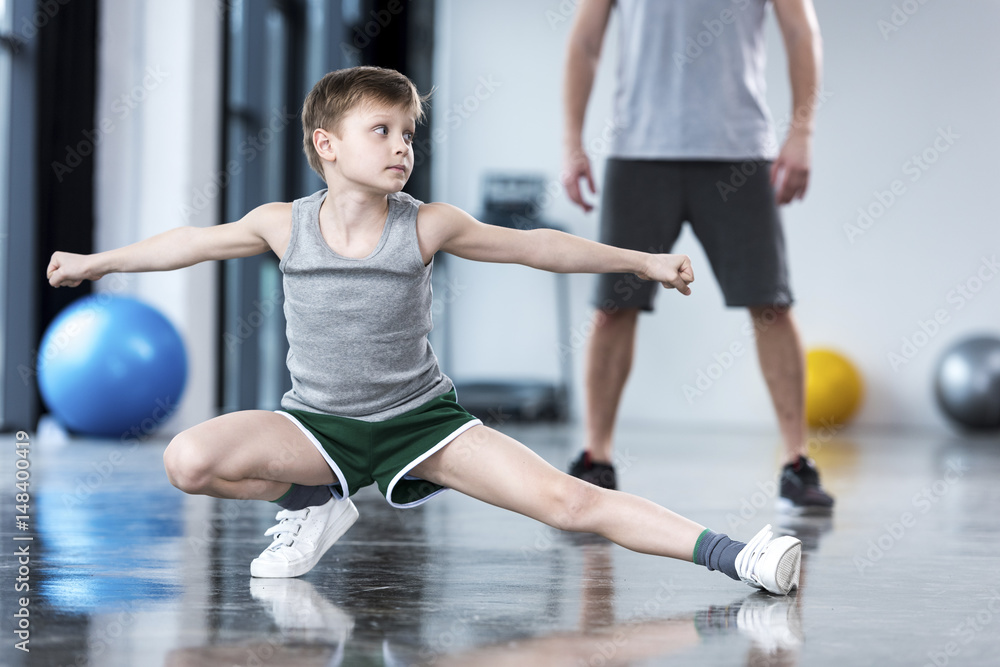 Coach controlling boy that doing stretching exercise at fitness center