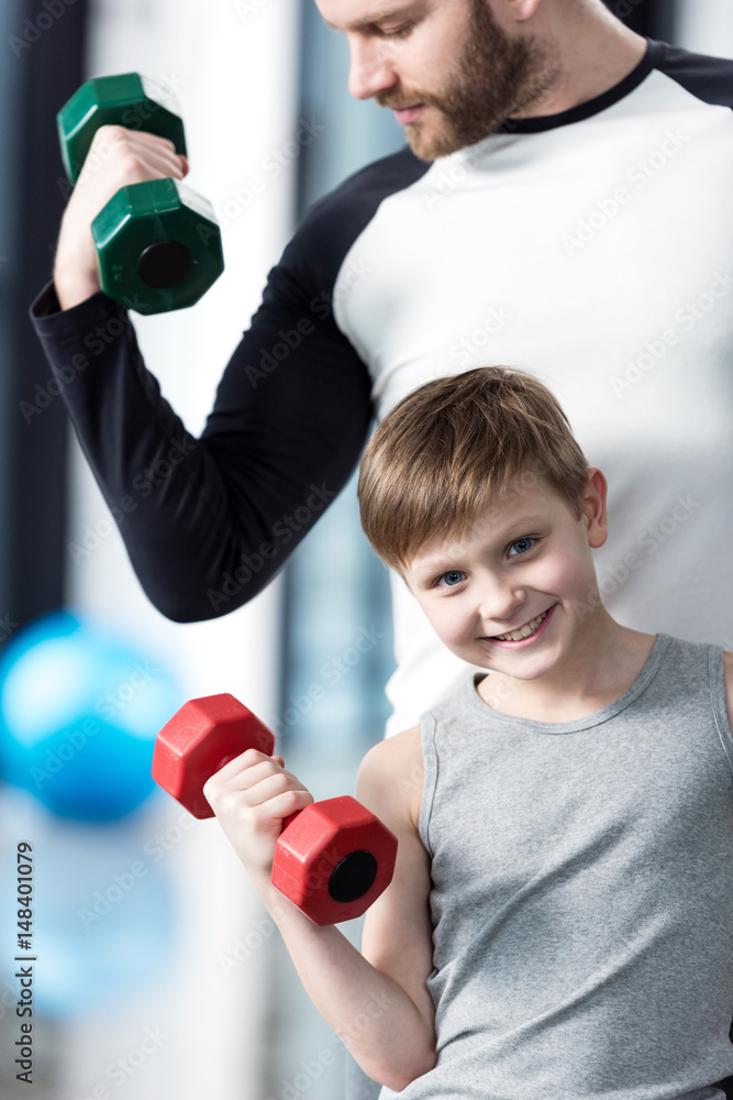 Boy training with dumbbells together with coach at fitness center