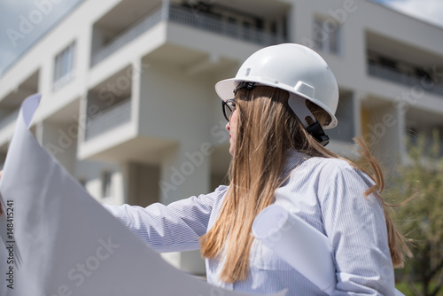 young architect holding blueprints looking at building in background 