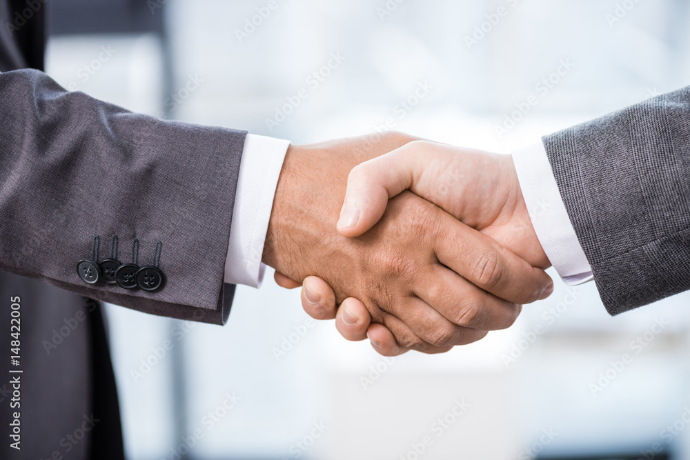 Close-up partial view of two businessmen in formal wear shaking hands, business concept