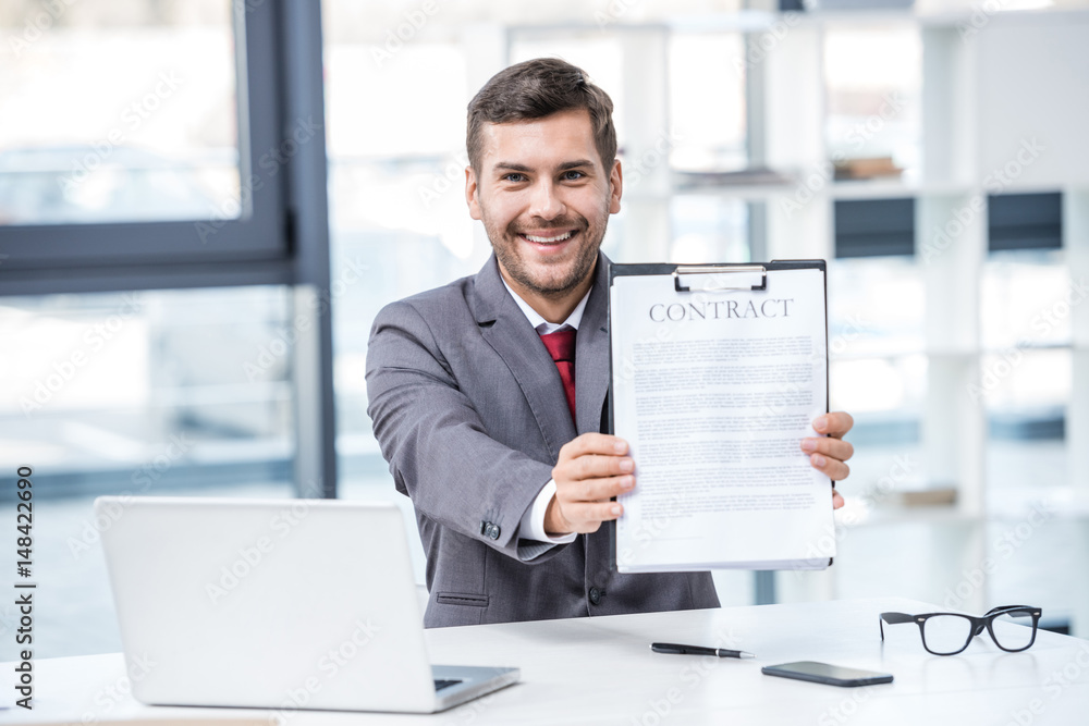 Handsome smiling businessman sitting at workplace and holding business contract, business concept Handsome smiling businessman sitting at workplace and holding business contract, business concept