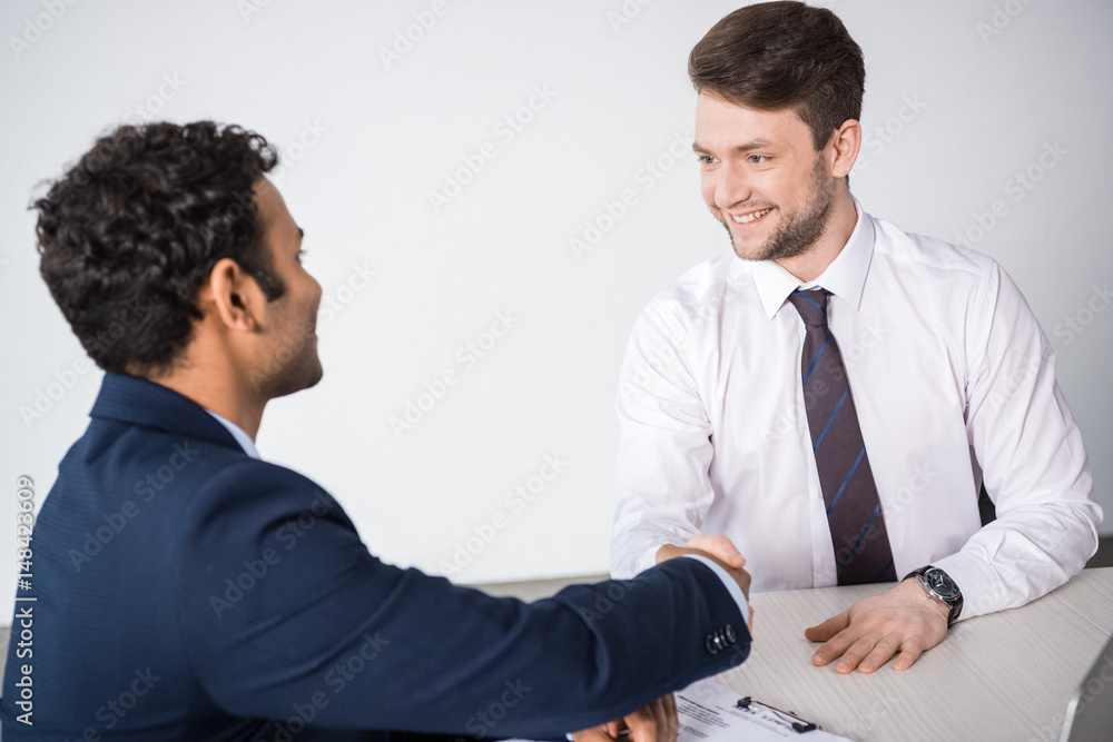side view of smiling businessmen shaking hands at workplace side view of smiling businessmen shaking hands at workplace