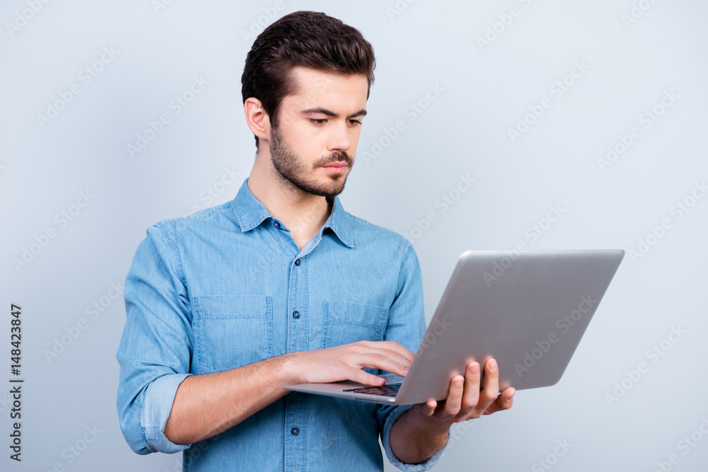 Portrait of concentrated young serious man typing on his laptop on light blue background Portrait of concentrated young serious man typing on his laptop on light blue background