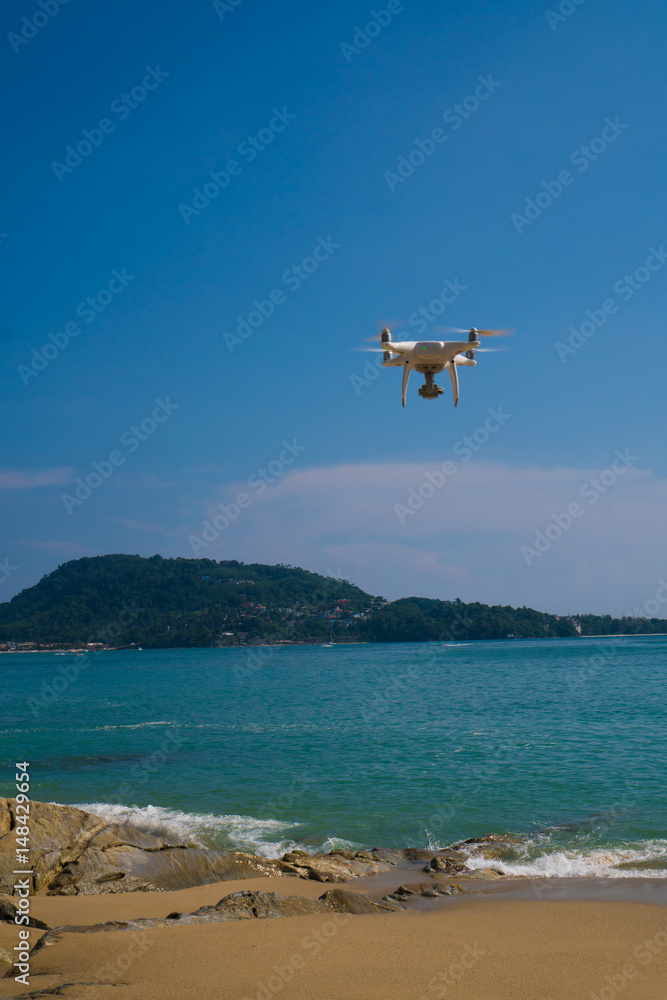 Flying drone above the beach with turquoise sea and blue sky background controlled by professional photographer