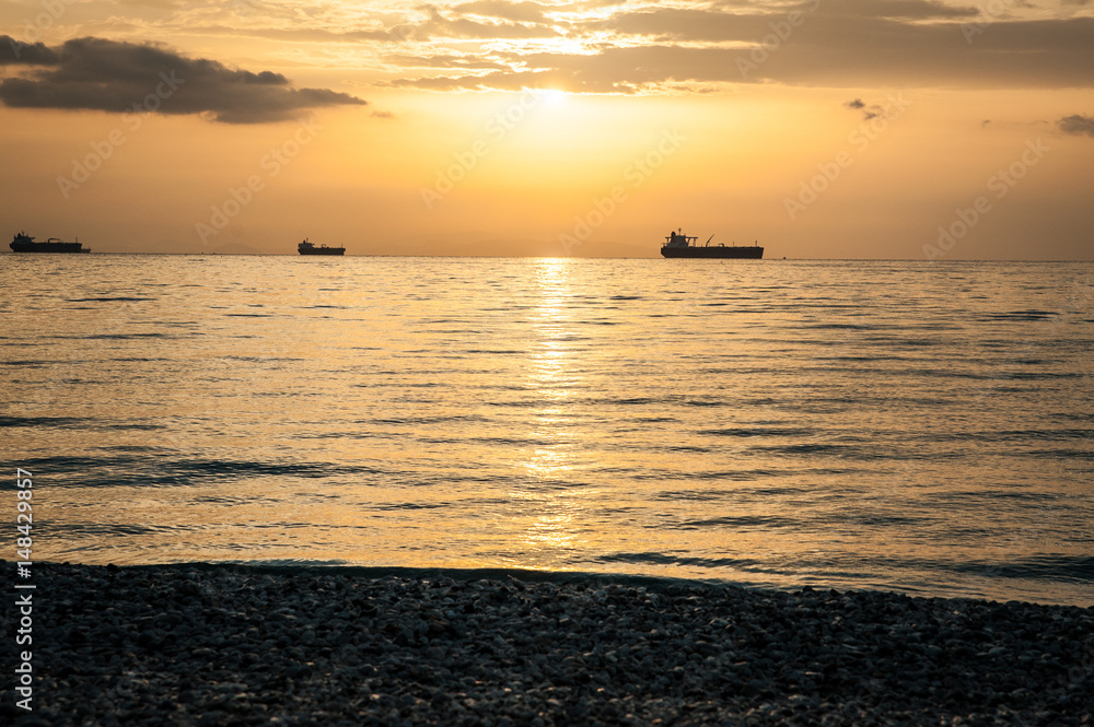 Beautiful orange sunset over the sea, landscape with ships and stone beach
