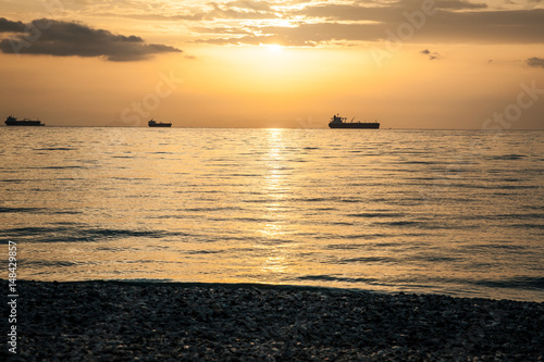 Obraz na płótnie Beautiful orange sunset over the sea, landscape with ships and stone beach w salonie