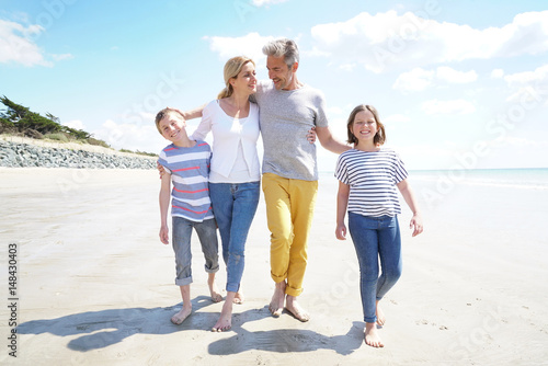 Happy family of four walking on sandy beach