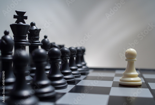 White pawn against the background of dark chess pieces photo