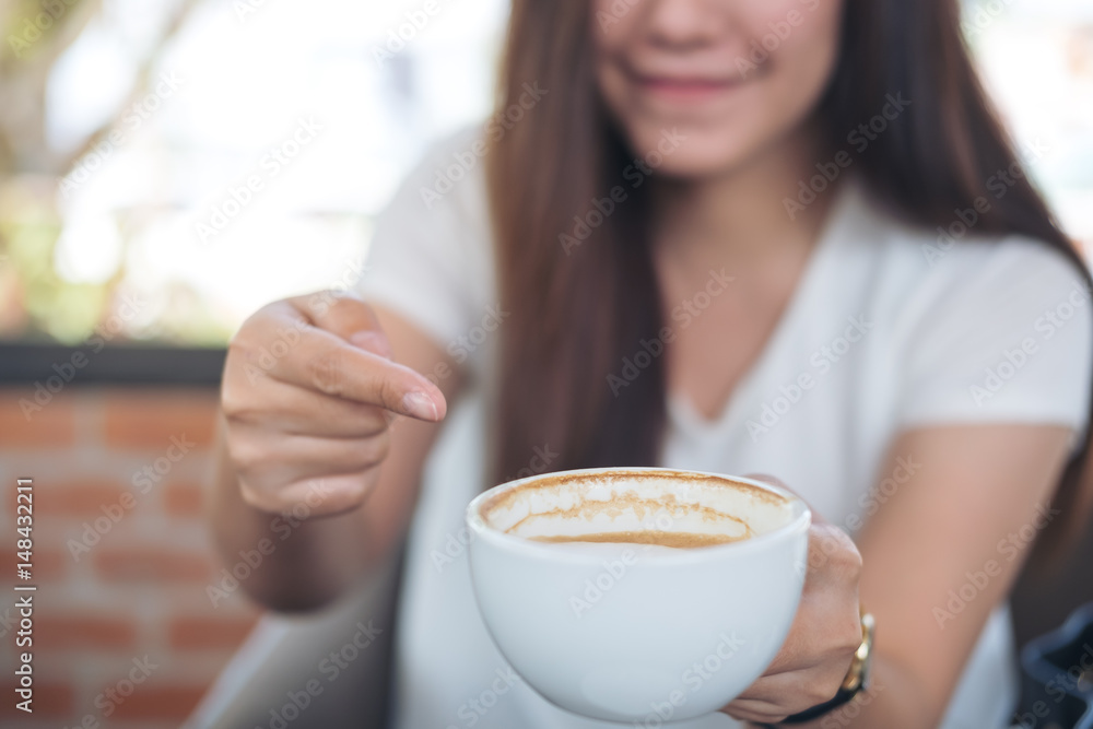 Closeup image of Asian woman holding and pointing at hot coffee with smiley face in coffee shop Closeup image of Asian woman holding and pointing at hot coffee with smiley face in coffee shop