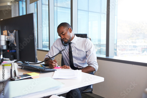 Businessman Making Phone Call Sitting At Desk In Office