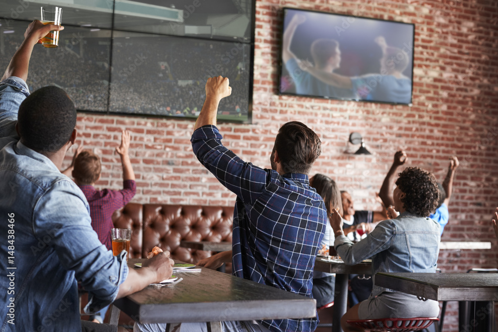 Friends Watching Game In Sports Bar On Screens Celebrating Stock Photo